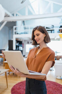 Schöne junge Geschäftsfrau mit braunen Haaren, die einen Laptop benutzt, während sie im kreativen Büro arbeitet - DIGF15389