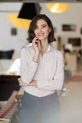 Lächelnde schöne weibliche Fachkraft mit Hand am Kinn im Büro stehend und wegschauend - DIGF15429