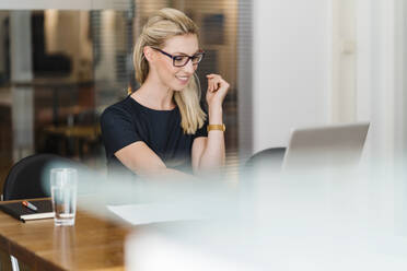 Lächelnde Unternehmerin mit Brille, die einen Laptop bei der Arbeit im Büro benutzt - DIGF15435