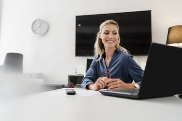 Lächelnde Unternehmerin bei der Arbeit im Büro am Laptop - DIGF15450