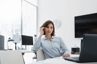 Junge Unternehmerin schaut bei der Arbeit im Büro auf ihren Laptop - DIGF15458