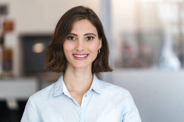 Schöne lächelnde junge weibliche Fachkraft mit braunen Haaren im Büro - DIGF15466