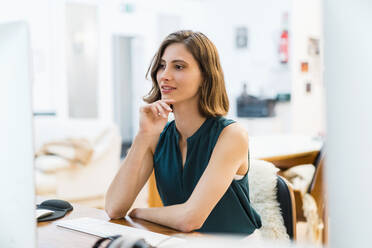 Young female entrepreneur sitting with hand on chin while working in office - DIGF15483