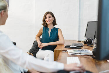 Lächelnde junge Geschäftsfrau, die eine Kollegin bei einer Diskussion im Büro anschaut - DIGF15485
