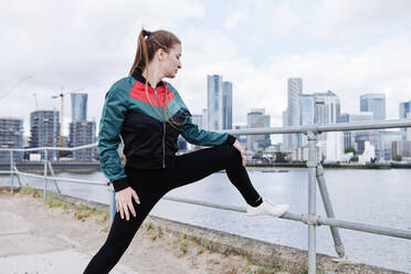 Fit woman doing stretching by river in city - ASGF00322