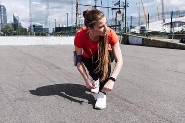 Sportlerin beim Schnürsenkelbinden auf der Promenade an einem sonnigen Tag - ASGF00330