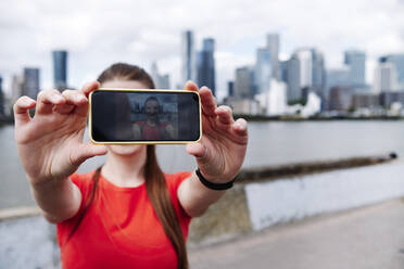 Mit dem Smartphone fotografierende Sportlerin in der Stadt - ASGF00334