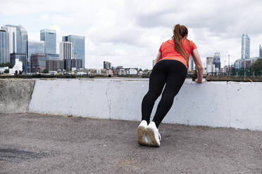 Weibliche Athletin beim Aufwärmtraining über einer Stützmauer in der Stadt - ASGF00336