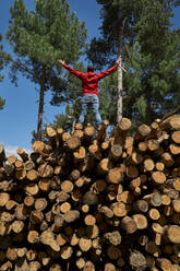 Mann mit ausgestreckten Armen auf Baumstämmen in der Holzindustrie stehend - VEGF04607