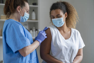 Curly haired woman receiving vaccine at medical clinic - SNF01467