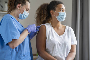 Curly haired woman with face mask getting vaccinated at hospital - SNF01469