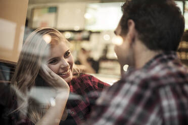 Smiling woman looking at boyfriend seen through cafe window - AJOF01373