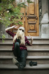 Lustige Frau mit Sonnenbrille, die auf einer Treppe sitzt und das Friedenszeichen zeigt - AJOF01383