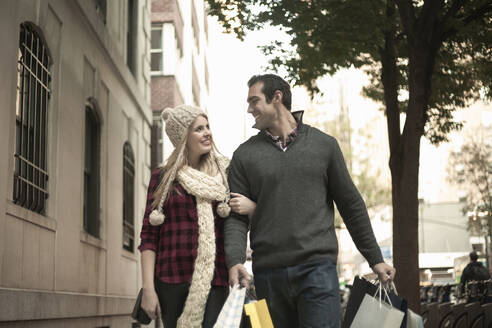 Lächelndes junges Paar mit Einkaufstaschen in der Stadt - AJOF01387