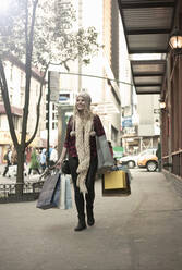 Junge Frau mit Einkaufstüten beim Spaziergang in der Stadt - AJOF01389