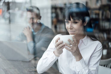 Thoughtful businesswoman holding coffee cup with colleague in background at cafe - JOSEF04570