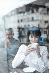 Smiling businesswoman looking through window with colleague sitting in background at cafe - JOSEF04582