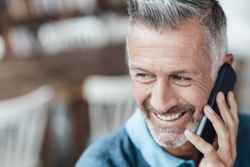 Älterer Geschäftsmann lächelt, während er in einem Café mit seinem Smartphone telefoniert - JOSEF04592