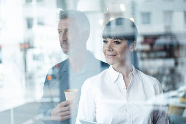 Geschäftsfrau schaut weg, während sie mit einem Kollegen im Hintergrund in einem Cafe steht - JOSEF04606