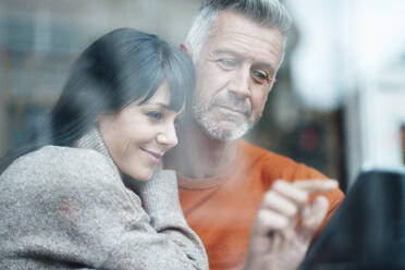 Smiling woman leaning on man's shoulder using digital tablet at cafe - JOSEF04662
