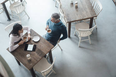 Männlicher Unternehmer hört einem Kollegen zu, während er in einem Café sitzt - JOSEF04669