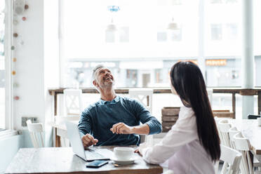 Smiling businessman looking at drone while sitting with colleague at cafe - JOSEF04675