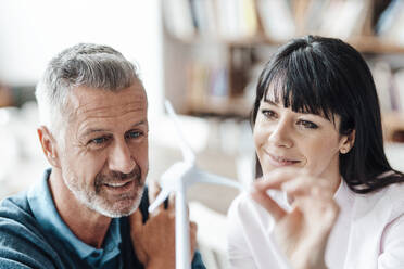 Smiling businesswoman checking wind turbine model with colleague at coffee shop - JOSEF04691