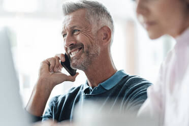 Smiling businessman talking on mobile phone by colleague at coffee shop - JOSEF04694