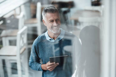 Lächelnder männlicher Unternehmer mit digitalem Tablet, der einen Kollegen in einem Café anschaut - JOSEF04699