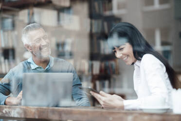 Männliche und weibliche Besitzer mit Laptop und Mobiltelefon lächelnd am Fenster des Cafés - JOSEF04708