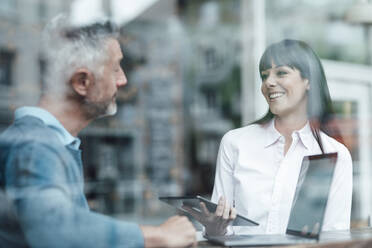 Female entrepreneur with digital tablet looking at colleague in coffee shop - JOSEF04709