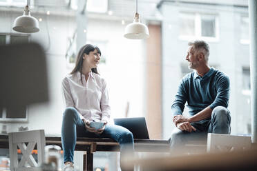 Female and male entrepreneurs smiling while sitting in coffee shop - JOSEF04714