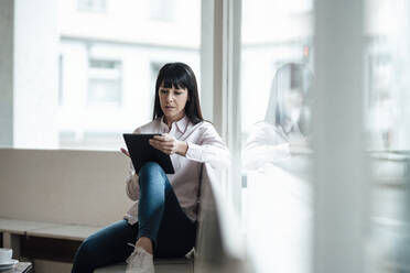 Weiblicher Besitzer, der ein digitales Tablet benutzt, während er am Fenster eines Cafés sitzt - JOSEF04716