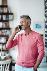 Male owner talking on mobile phone while standing in coffee shop - JOSEF04724