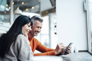 Smiling mature couple using smart phone at cafe - JOSEF04774