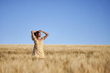 Cheerful woman standing at wheat field in front of blue sky - KIJF03928