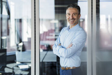 Smiling male entrepreneur standing with arms crossed at doorway in office - DIGF15518