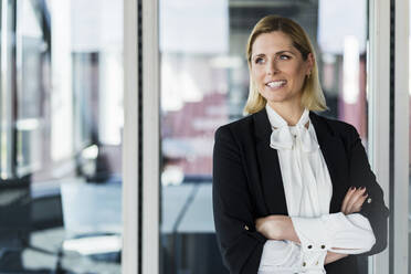 Blond businesswoman standing with arms crossed in office - DIGF15524