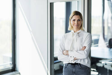 Blond businesswoman standing with arms crossed at office - DIGF15527