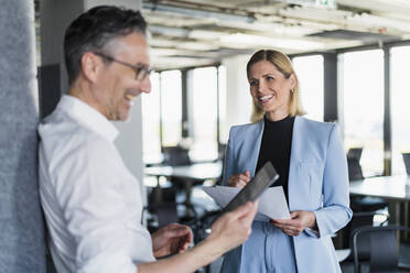 Smiling female entrepreneur looking at male colleague using digital tablet in office - DIGF15553