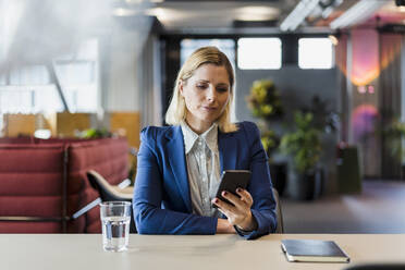 Unternehmerin, die am Schreibtisch im Büro sitzt und über ihr Smartphone Textnachrichten verschickt - DIGF15566