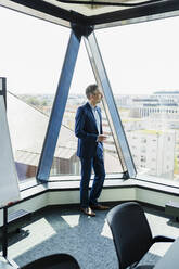 Männlicher Unternehmer steht im Sitzungssaal und schaut durch ein Fenster - DIGF15593
