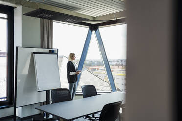 Businesswoman standing by glass window in board room - DIGF15594