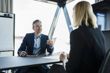 Mature businessman discussing with female colleague while sitting in board room - DIGF15598