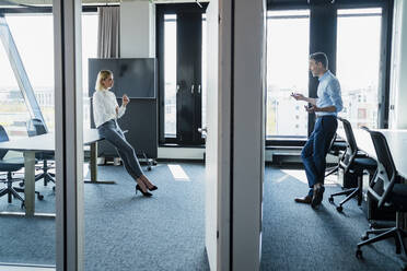 Älterer Geschäftsmann gestikuliert, während er mit einer Frau diskutiert, die auf einem Schreibtisch im Büro sitzt - DIGF15605