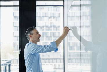 Male entrepreneur writing on white board while working in office - DIGF15606