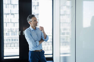 Thoughtful businessman looking at white board while planning strategy in office - DIGF15608