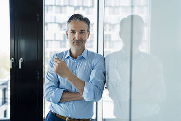 Male entrepreneur leaning on white board while standing in office - DIGF15609