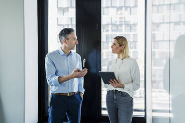 Businesswoman holding digital tablet looking at male coworker discussing strategy in office - DIGF15612