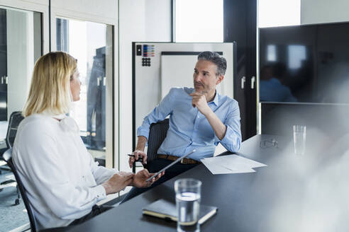 Älterer Geschäftsmann schaut auf eine Unternehmerin, die im Büro sitzt und diskutiert - DIGF15616